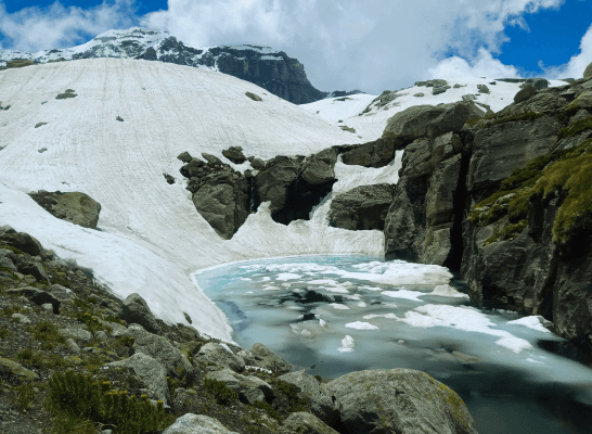 Glacial lake lies half-frozen amid snowy slopes